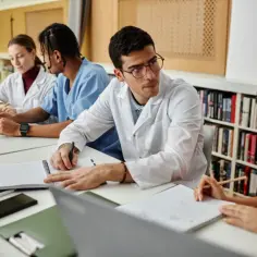Studenci dyskutują, czy warto wybrać prawo medyczne jako specjalizację po aplikacji. W tle regały z książkami.