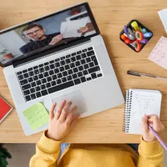 Dziecko uczy się zdalnie przy laptopie, pisząc notatki w zeszycie.