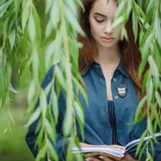 Dziewczyna z rudymi włosami, czytająca książkę pod płaczącą wierzbą. Idealna sceneria na matura z biologii od zera.