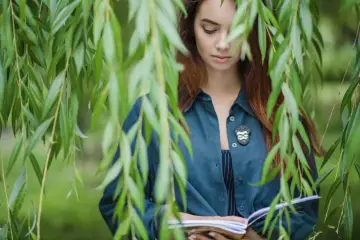 Dziewczyna z rudymi włosami, czytająca książkę pod płaczącą wierzbą. Idealna sceneria na matura z biologii od zera.